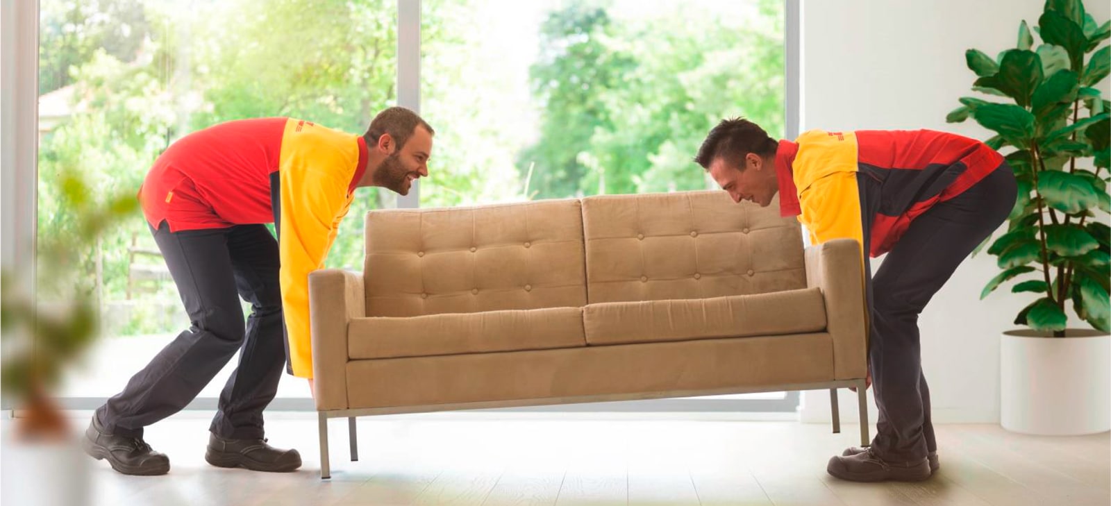 DHL 2-Mann-Serivce Symbolbild mit 2 Männern, die ein Möbelstück in die Wohnung tragen und absetzen.